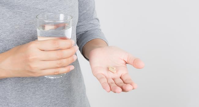 person holding 2 magnesium breakthrough capsules and a glass of water